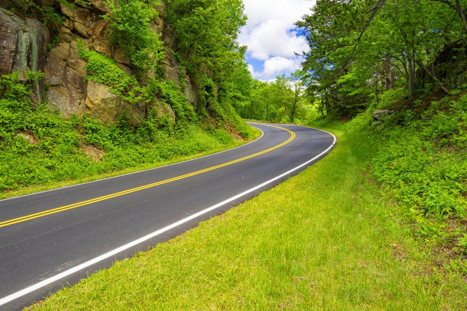 Winding road through lush green hills under a bright blue sky.