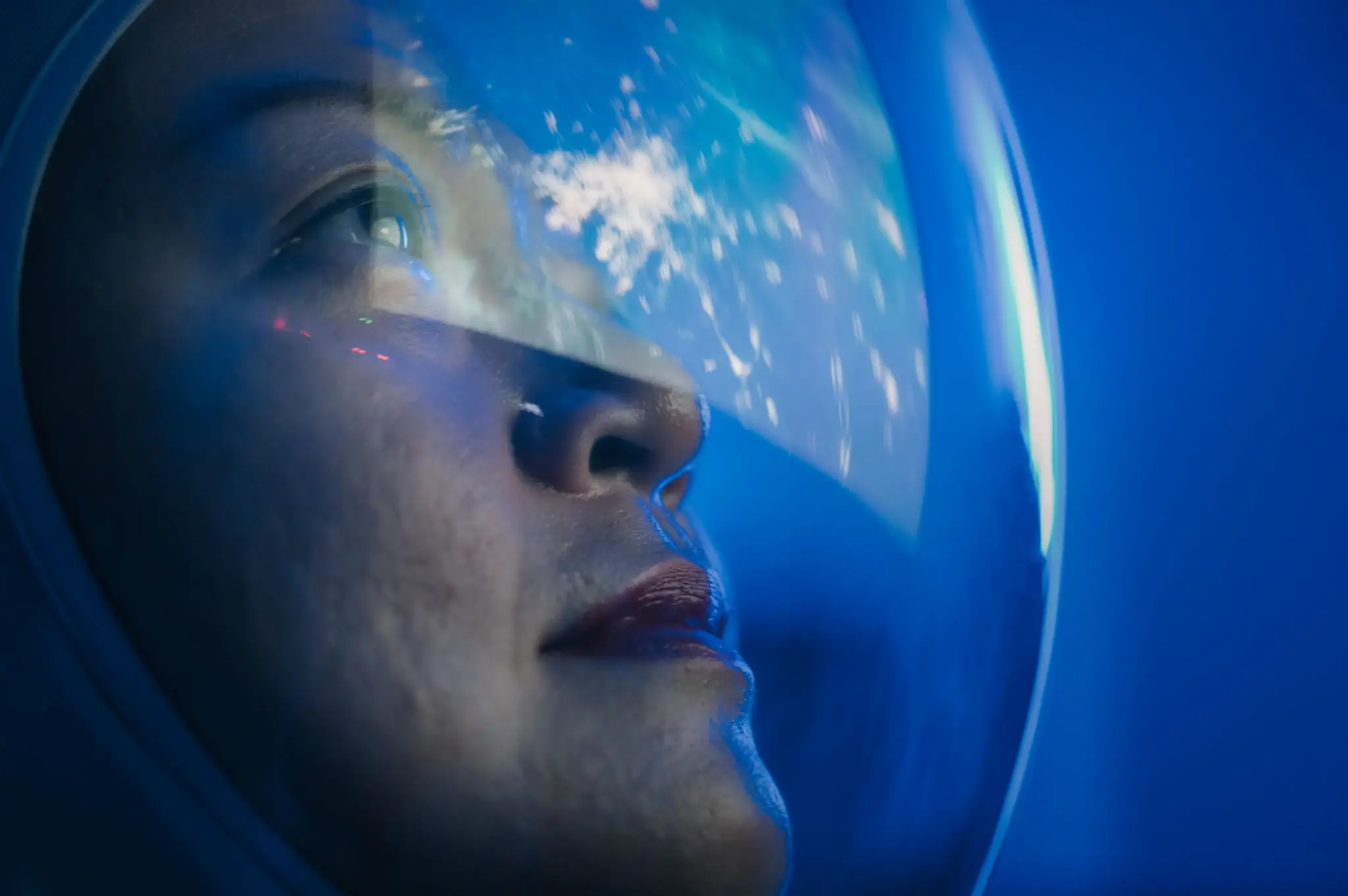 Close-up of a person wearing a space helmet, gazing thoughtfully.