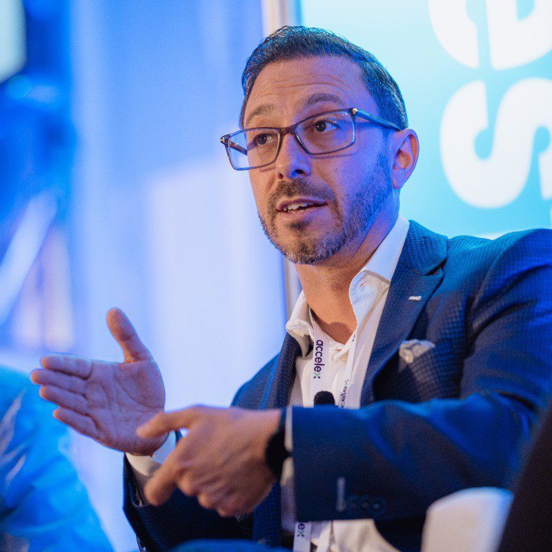 Man wearing glasses speaking and gesturing during a discussion.