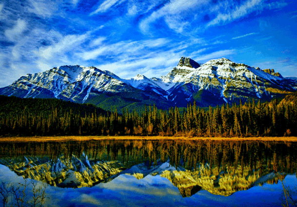 Snow-capped mountains reflected in a calm lake under a vibrant blue sky.
