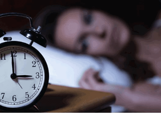 A woman lying awake in bed with an alarm clock in focus.